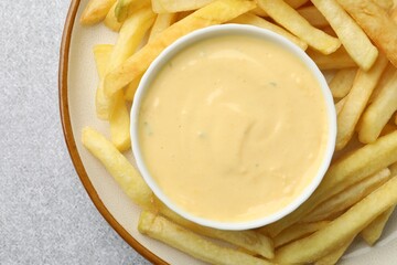 Tasty cheese sauce in bowl and French fries on grey table, top view