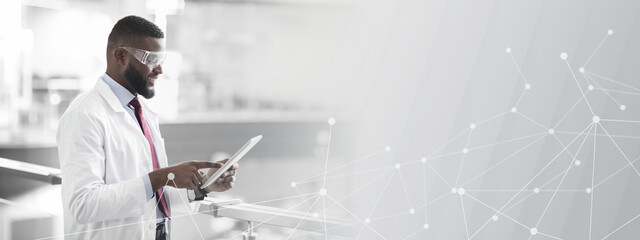Cheerful african american guy in workwear and protective glasses medical scientist using digital tablet, analyzing data, posing at workplace, panorama with copy space. Jobs and occupations concept