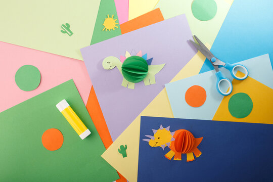 Colorful sheets of paper in various shades. Two playful 3D dinosaur crafts. DIY children craft and creative hobby for toy stores, art schools, and kindergartens