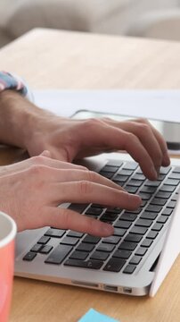 Close-up of man hands working from home, typing on a laptop keyboard. Focused on messaging and texting, he efficiently manages tasks. Vertical video.