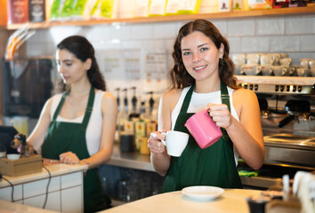 Young woman barista pouring freshly brewed coffee into cup in cafe