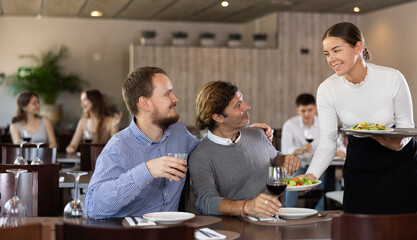 Young woman waitress takes order from couple young man and adult man in restaurant..