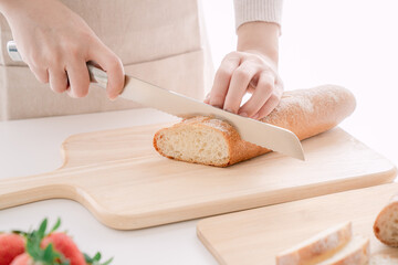 Close-up of hand slicing a crusty baguette with a serrated knife on a wooden cutting board