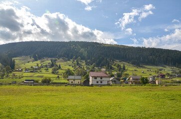Beautiful rural landscape featuring a Verkhovyna village with houses, nestled amid green meadows...