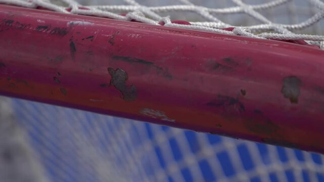 Close up panning shot of dek hockey rink net pipe with scratches, dents, and paint flicking off during the spring summer time