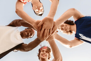 Sports unity concept. Multiracial sportsmen putting their hands together before basketball game outside, bottom view