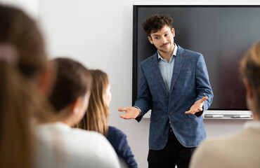 Positive skilled male coach explaining topic to group of people during foreign language class in...