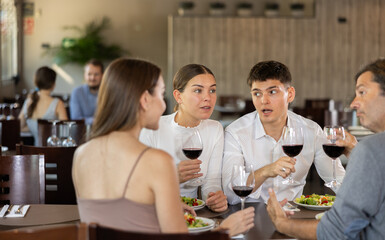 Two couples of men and women drinking eating and talking in restaurant