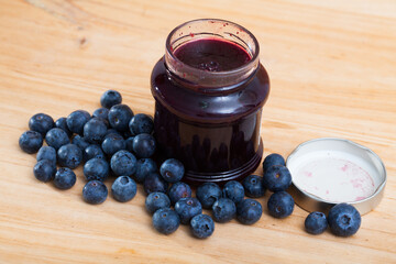 Image of tasty blueberry jam in jar and fresh berries on wooden surface