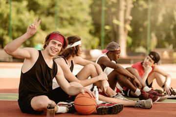 Happy young basketball player and his multinational team having rest at outdoor arena, copy space....