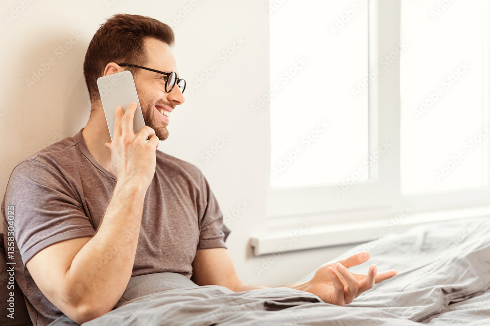 Poster happy man talking on mobile phone calling somebody having cellphone conversation sitting in bed in b