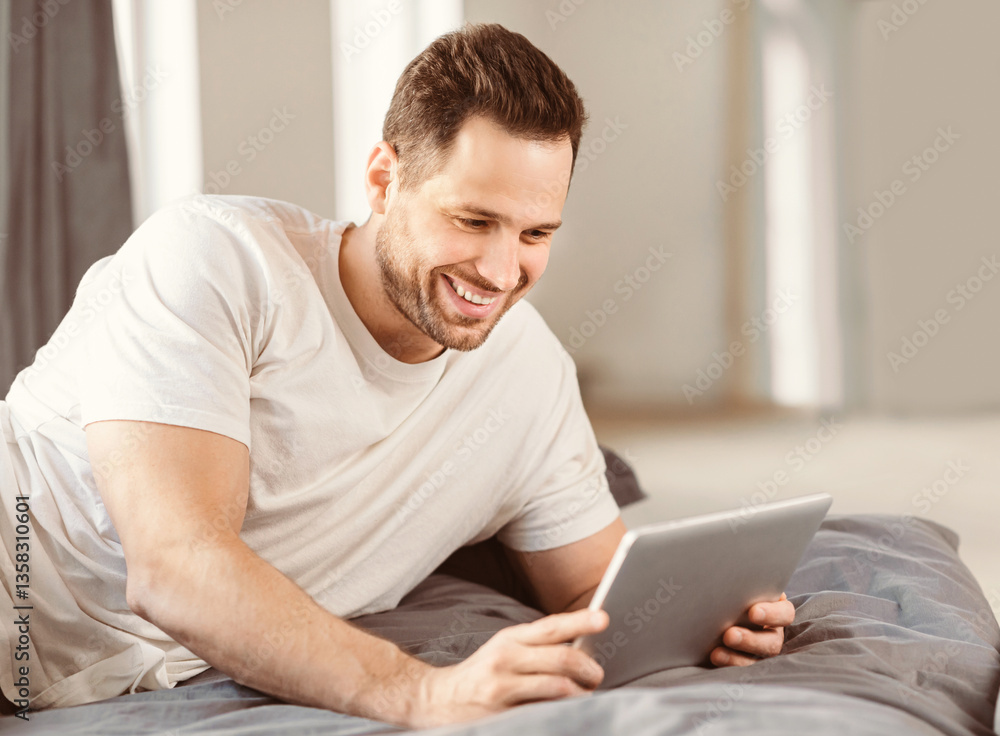 Aufkleber cheerful man using digital tablet watching movie relaxing lying in bed at home. weekend morning conc