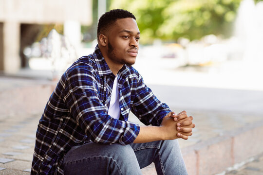 Portrait of cool african american guy sitting on the steps, looking away and thinking, copy space