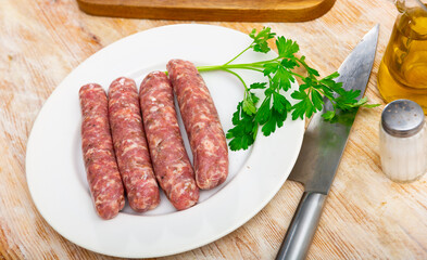 Fresh raw pork botifarra sausages ready for grilling on plate with kitchen knife and greens. Catalan cuisine