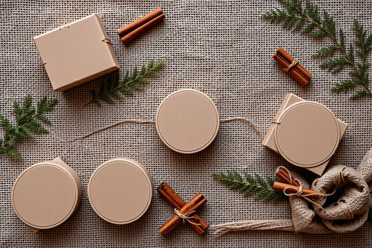 Neutral toned boxes and containers, cinnamon sticks, and green twigs arranged on a burlap surface create a rustic, natural, and earthy scene.