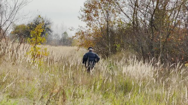 An old man walks through the thickets in a field