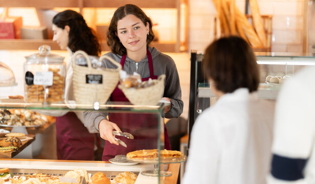 Cafeteria young woman worker sells fresh pastries, serves customers. Crowd was queuing at snack bar. Queue of customers is lined up at counter of bakery.