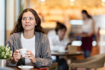 Young woman drinking fresh coffee at table in cafe