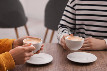Coffee break. Women with cups of hot drinks at wooden table indoors, closeup
