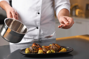 Professional chef adding sauce to delicious dish at table indoors, closeup