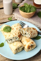 Tasty rolled crepes with cottage cheese and spinach served on wooden table, closeup