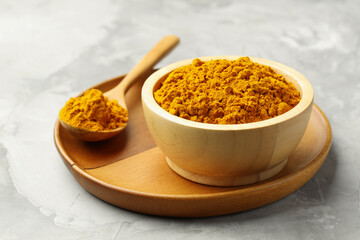Turmeric powder in bowl and spoon on light grey table, closeup