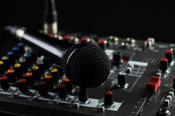Professional mixing console with microphone on black background, closeup