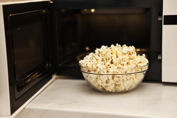 Tasty popcorn in bowl near microwave oven on white marble countertop indoors