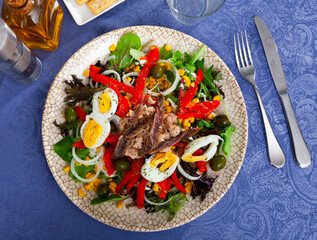 Corn, olive, anchovy, pepper, lettuce salad served on white plate.