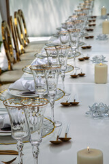 table deco event, crystal glasses, cutlery , white tablecloth and lit candles, gold accents on the decorations