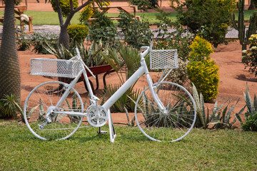 Fototapeta premium vintage bicycle painted white ,garden deco, creativity in decoration of landscaped land, green lawn and wood benches