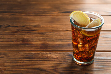 Refreshing iced cola with lemon slices on wooden table. Space for text
