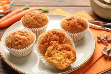 Tasty carrot muffins, fresh vegetables and walnuts on wooden table, closeup