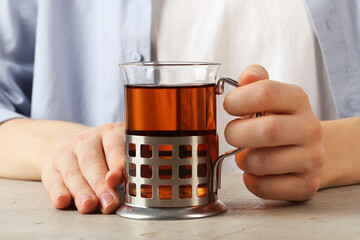 Woman with glass of tea in metal holder at beige table, closeup