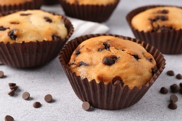Delicious muffin with chocolate chips on light grey table, closeup