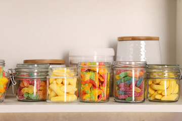 Tasty gummy candies in jars on shelf