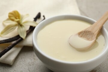 Tasty condensed milk, vanilla pods, flower and spoon on light grey table, closeup