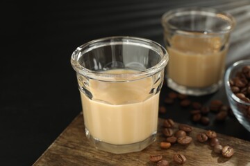 Coffee cream liqueur in glasses and beans on black table, closeup