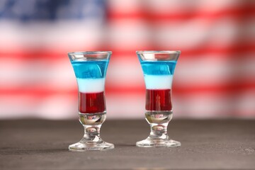 Tasty cocktails in shot glasses on grey table against flag of USA
