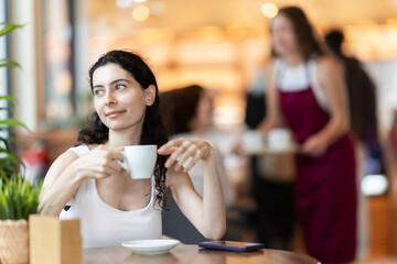 Young woman drinking fresh coffee at table in cafe