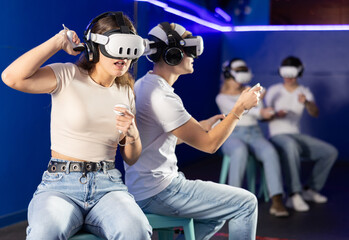 Guy and a girl in a virtual reality helmet are actively playing a video game against another...