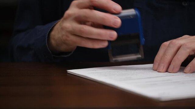 close-up male hands signing an official document and putting seal. businessman signs an agreement or contract while sitting at his desk. concept business document management. front view.