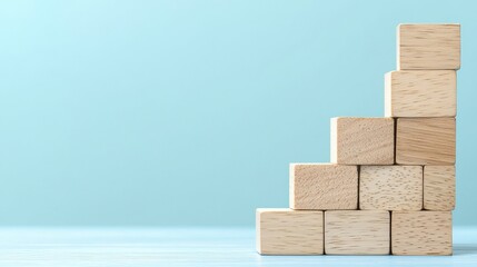 Obraz premium A minimalist arrangement of wooden blocks stacked in a stair-like formation against a light blue background.