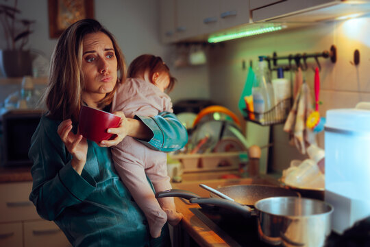 Mother Drinking Coffee and Cooking while Carrying Baby. Overworked mom multitasking in the kitchen while babysitting 

