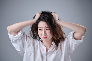 Fototapeta premium A young woman with disheveled long hair holds her head with both hands, looking troubled.