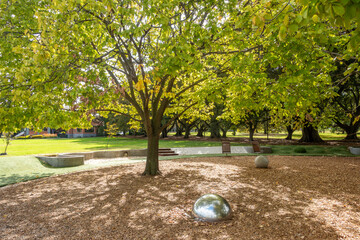 An artistic urban landscape with public seating benches and a reflective metallic sphere sculpture in a public park in Melbourne, Australia. A community green space or well-maintained parkland.