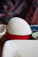 White egg resting in a red bowl among colorful dishes