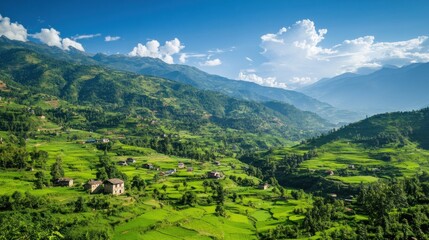 Fototapeta premium Lush green mountain valley with terraced fields and small houses under a bright blue sky.