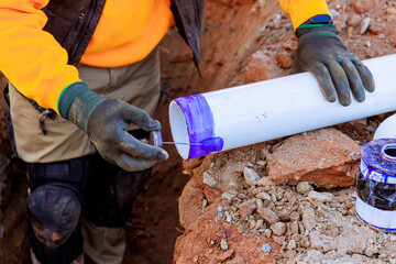 Construction worker prepares PVC piping by applying purple primer to ensure durable seal in trench...