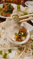 Close-up of a dumpling being held by chopsticks. A sauce and bean sprouts are visible in the background, creating a vibrant and appetizing food scene.